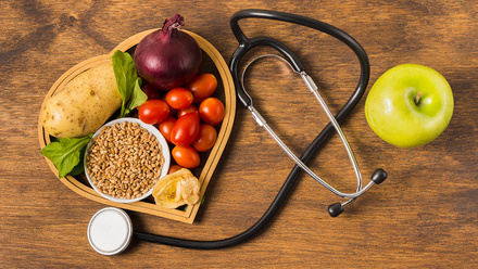 Heart shaped plate of plant-based foods next to a stethoscope and an apple.